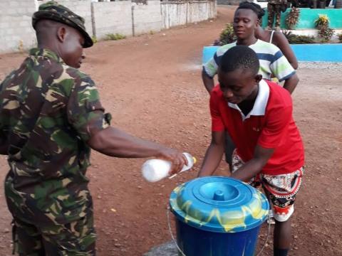 A military officer supervises a hand washing point at a border in eastern Sierra Leone