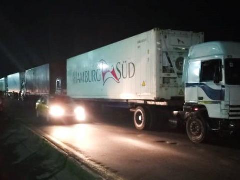 Trucks carrying loaded containers parked along Bia Burreh Road at night.